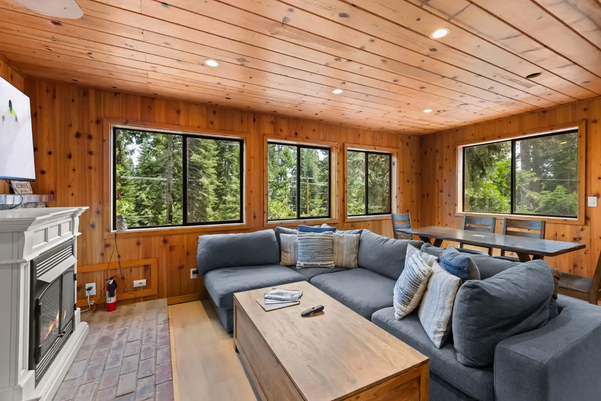 Gray sectional and fireplace in a pine-paneled room, Homewood Cabin in the Pines