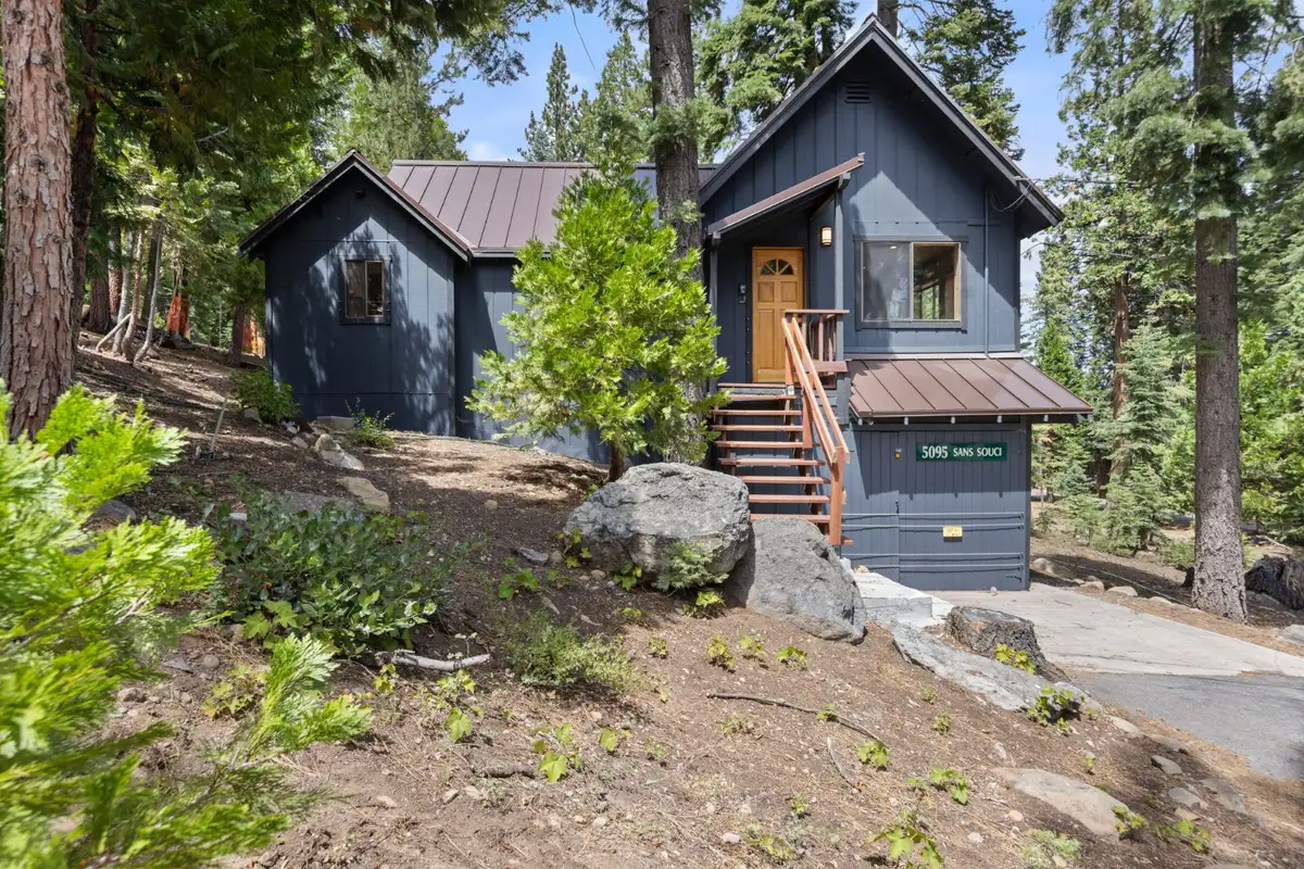Dark blue cabin with a metal roof and front stairs among pines, Homewood Cabin in the Pines