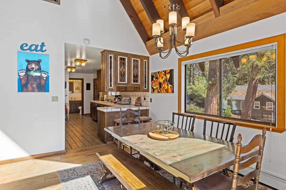 Dining table by a large window with kitchen beyond, Rustic Ridge Retreat