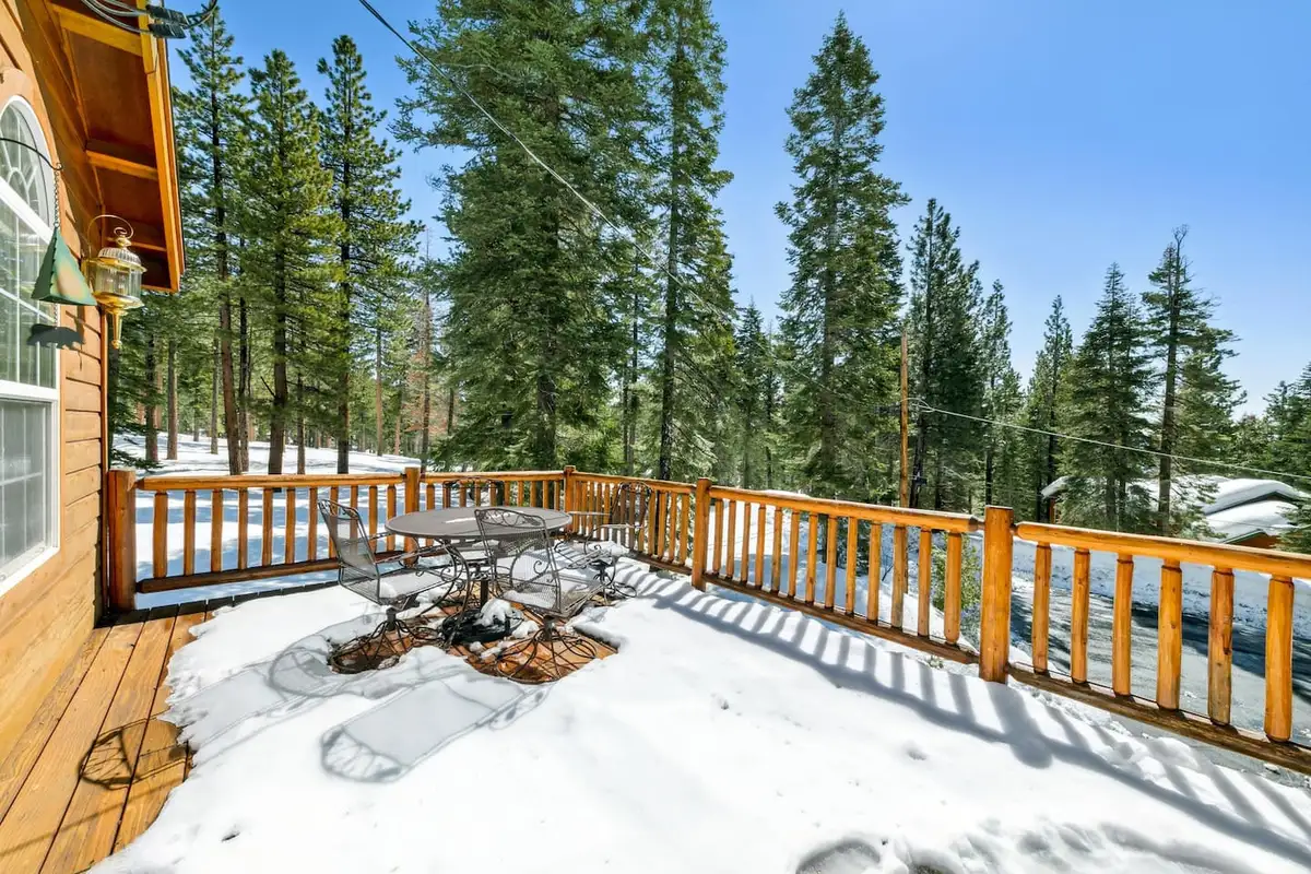 Snow-covered deck with log railings among pine trees, Hastings Hideaway Cabin