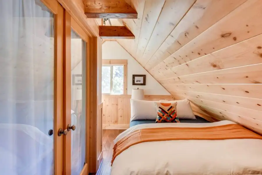 Bedroom with a sloped pine ceiling seen through glass doors, Tranquil Trails Cabin