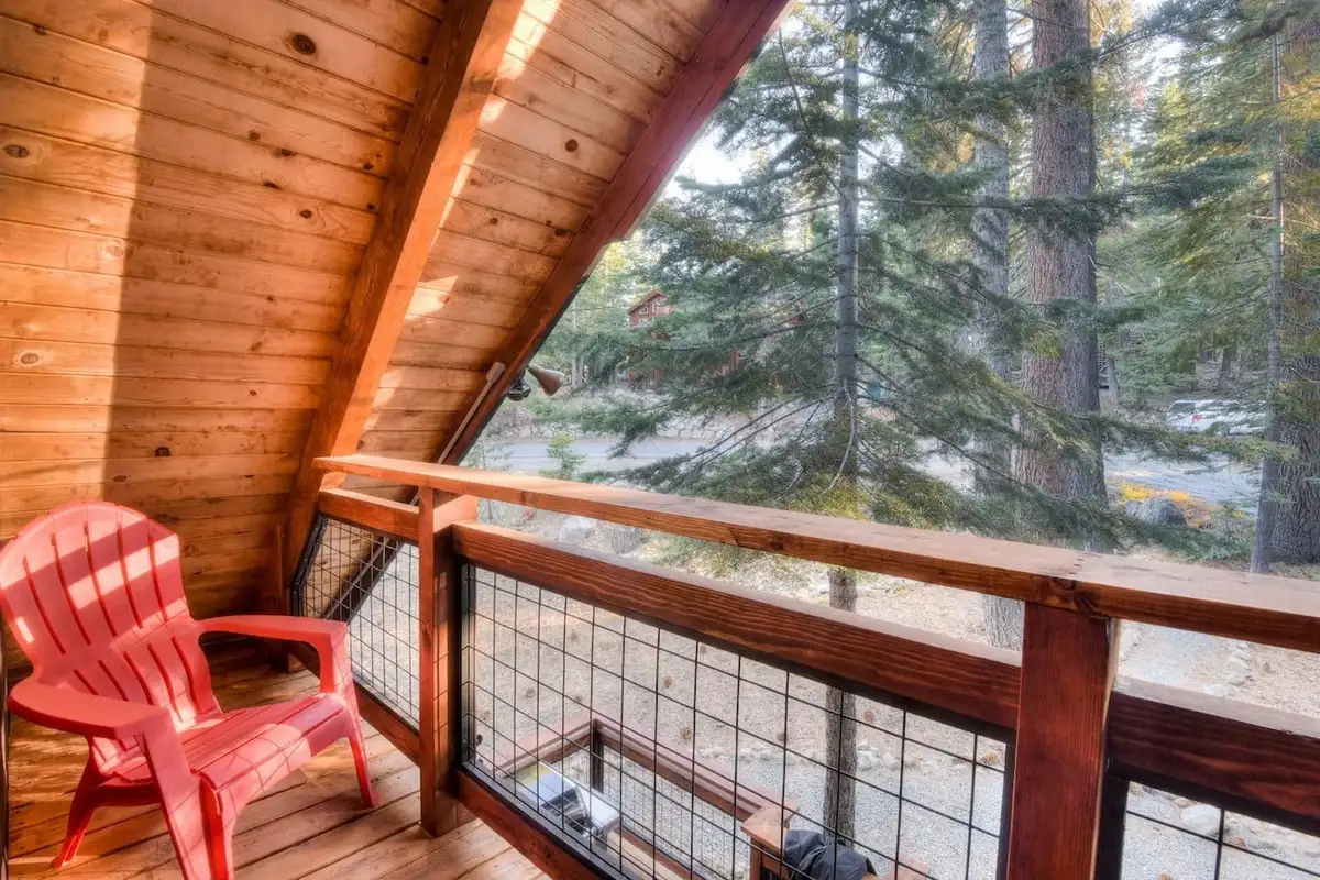 Balcony with a red chair and wire railing facing pines, Enchanting Chamberlands Cabin